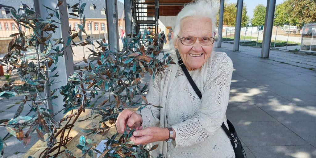 Eine Dame bringt ein Blatt am Paradiesbaum an.